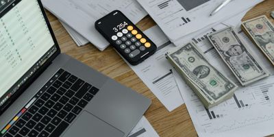 Laptop, phone, and documents with tables, charts, and columns of bank statement transactions