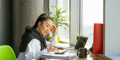 Asian woman at desk calculating local district sales tax on calculator