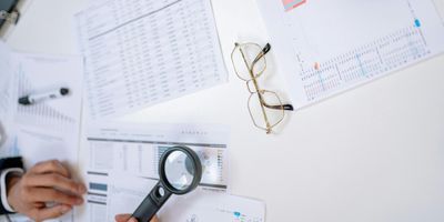 Sales tax analysis sheets laid out on table being examined with a magnifying glass