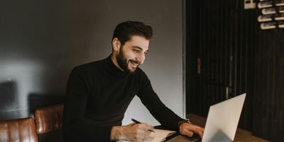 Entrepreneur writing on notebook in front of laptop