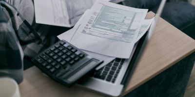Laptop, tax forms, and calculator on a wooden arm rest